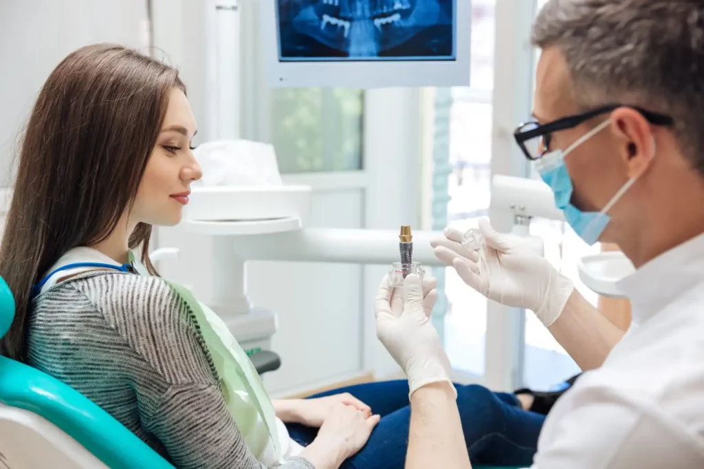 Male dentist showing a dental implant model to a patient. Expert restorative dental care from a Falls Church Dentist at Broadway Dental Associates.