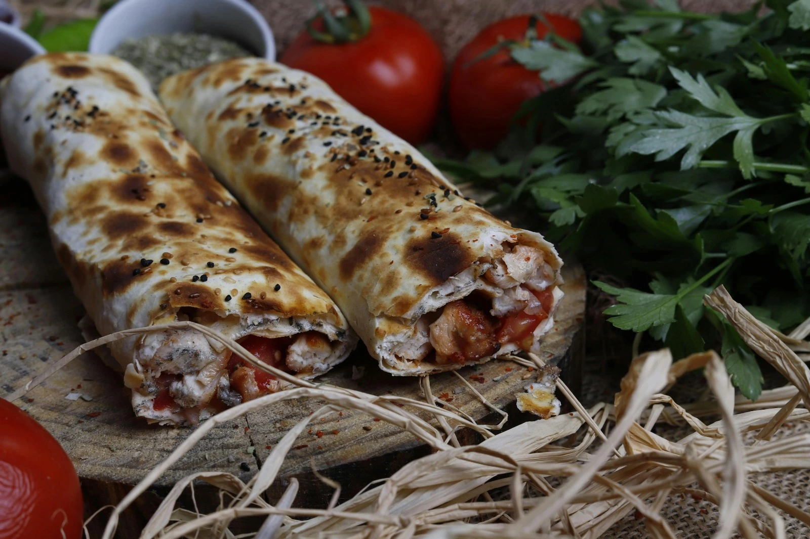 Two tasty Mediterranean wraps are served, and behind them are also tomatoes and greens.