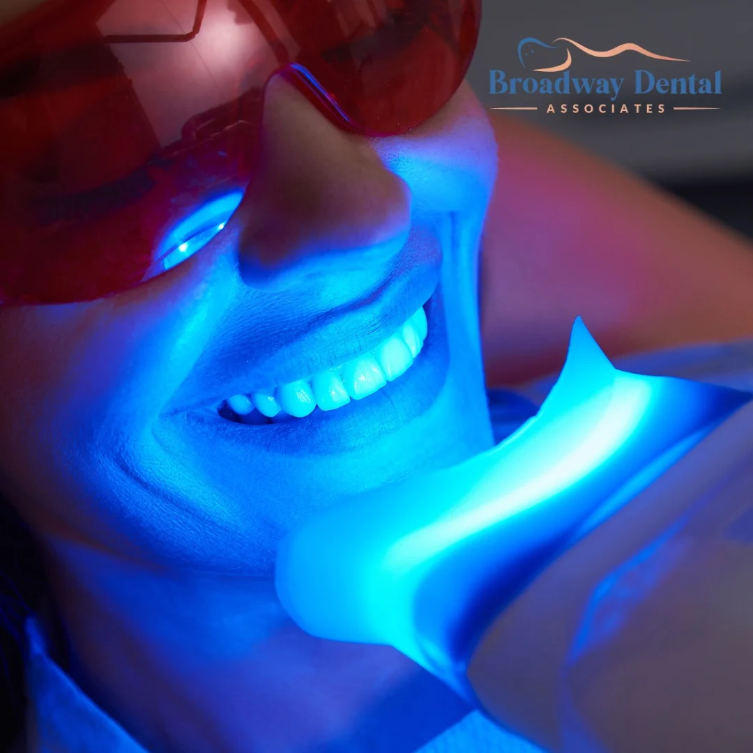 A patient with protective glasses getting their teeth whitened by a blue light, illustrating dental care
