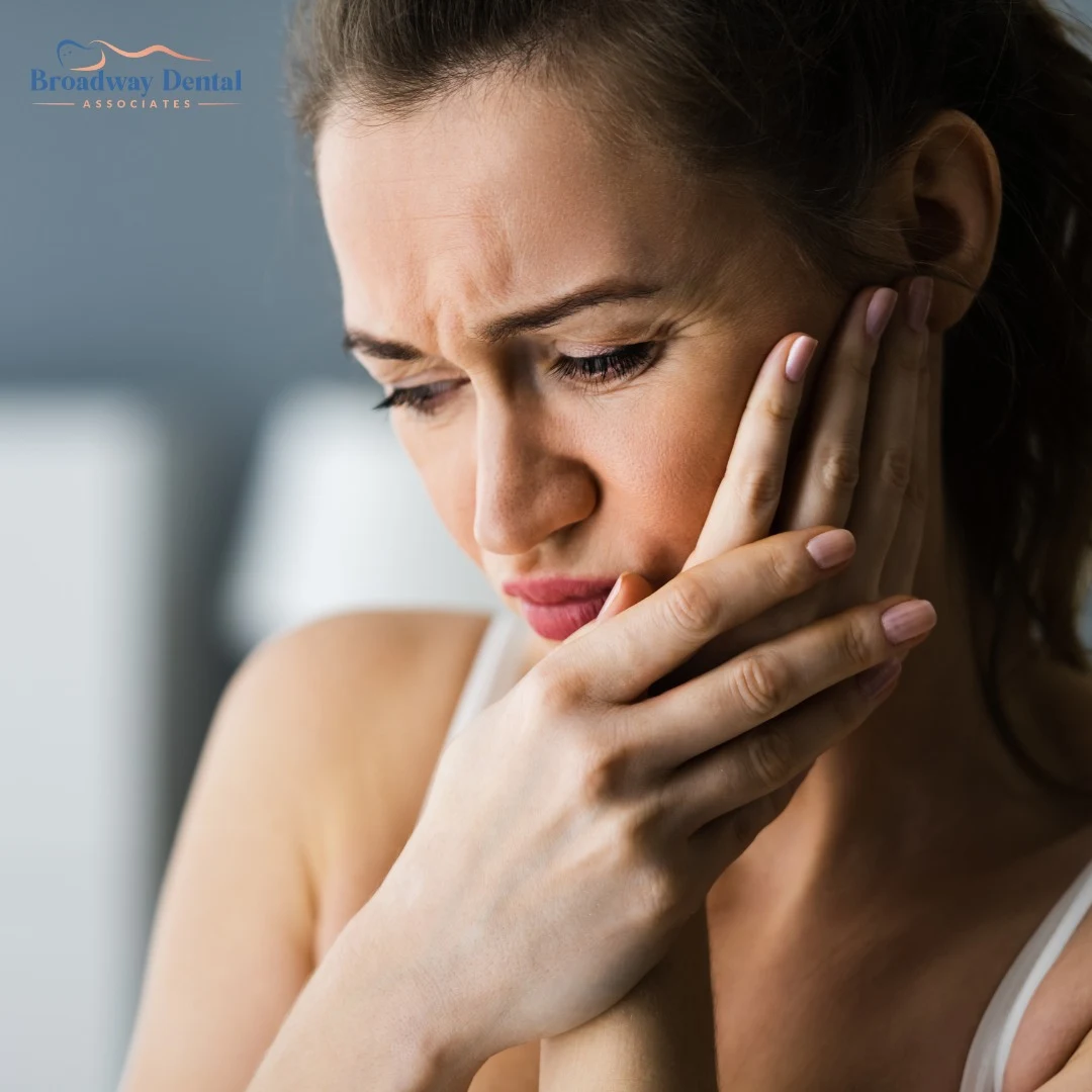 A young woman wearing lipstick holds her jaw in pain