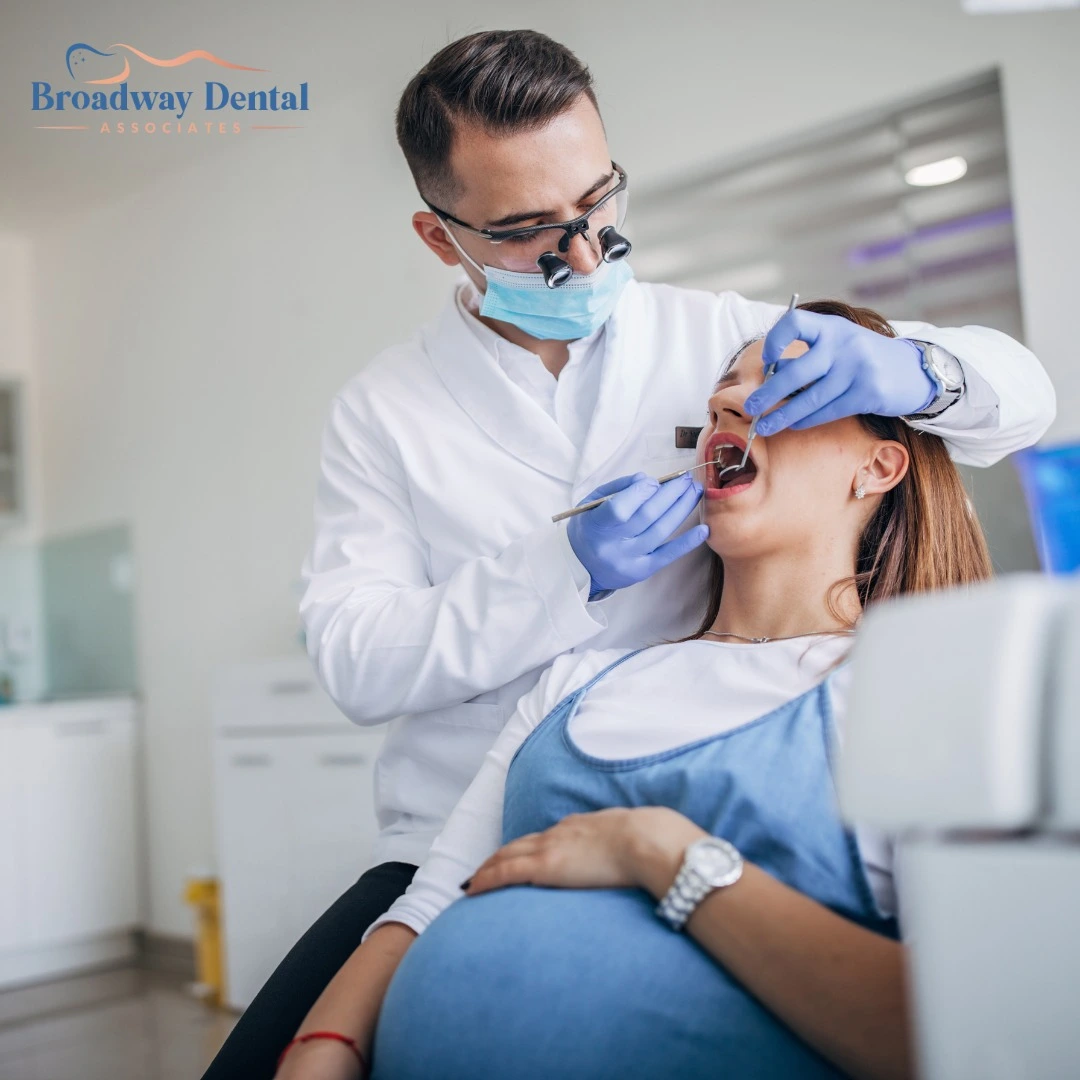 Pregnant woman in a white and blue dress receiving a dental checkup from a male dentist wearing magnification loupes and blue gloves