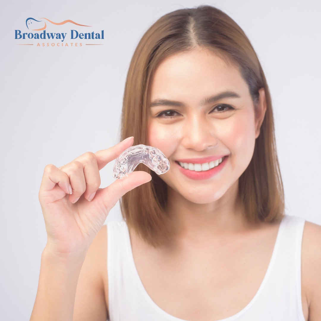 A young, smiling woman holds up her clear aligner