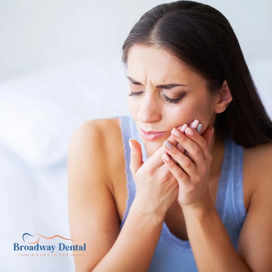 Woman holding her aching cheek in discomfort and Broadway Dental Associates logo in the bottom left of the image