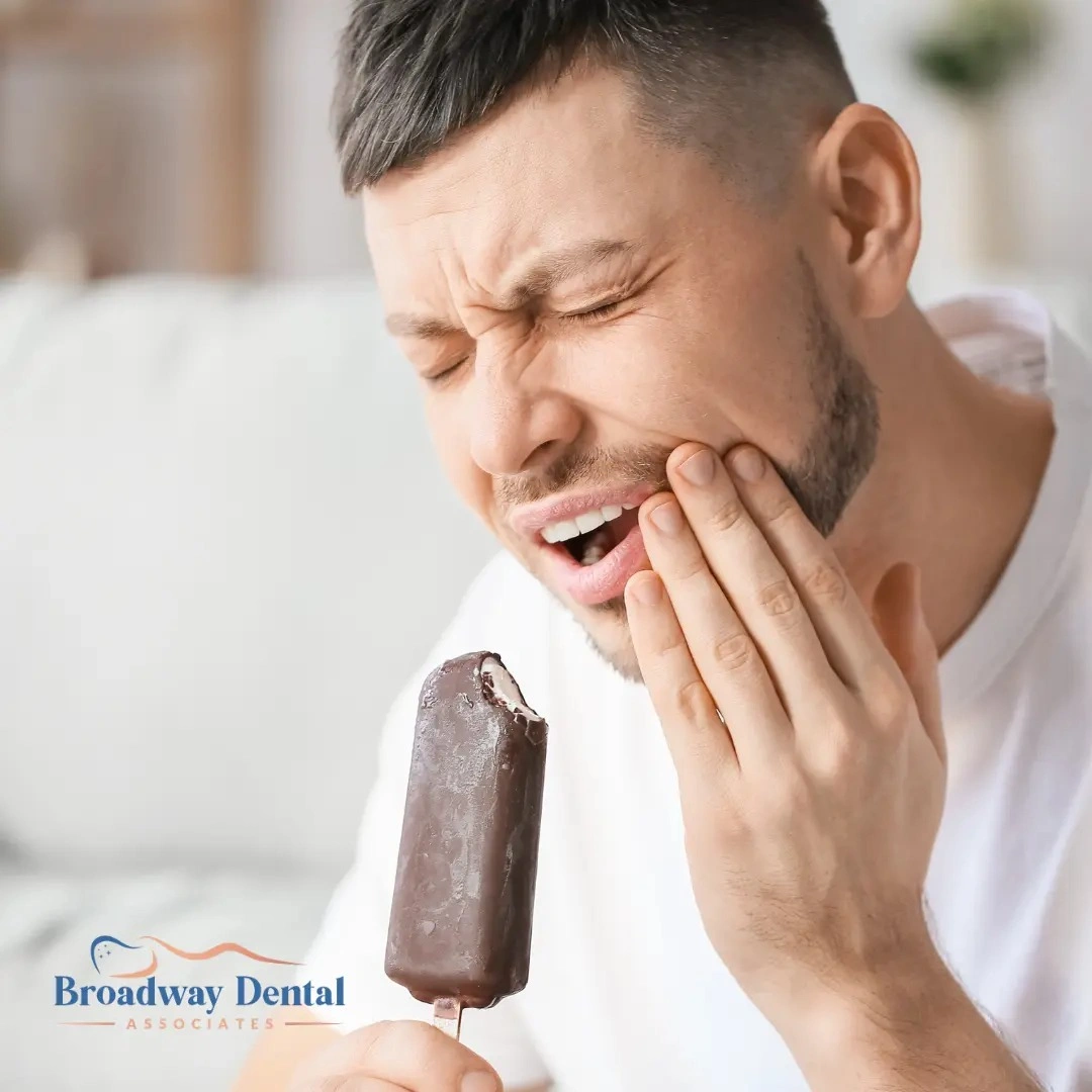 Man flinching with tooth pain eating ice cream and Broadway Dental Associates logo in the bottom left of the image.