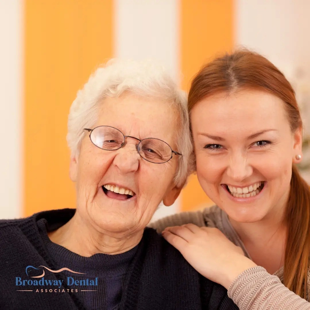 Senior woman and adult daughter smiling together and Broadway Dental Associates logo in the bottom left of the image