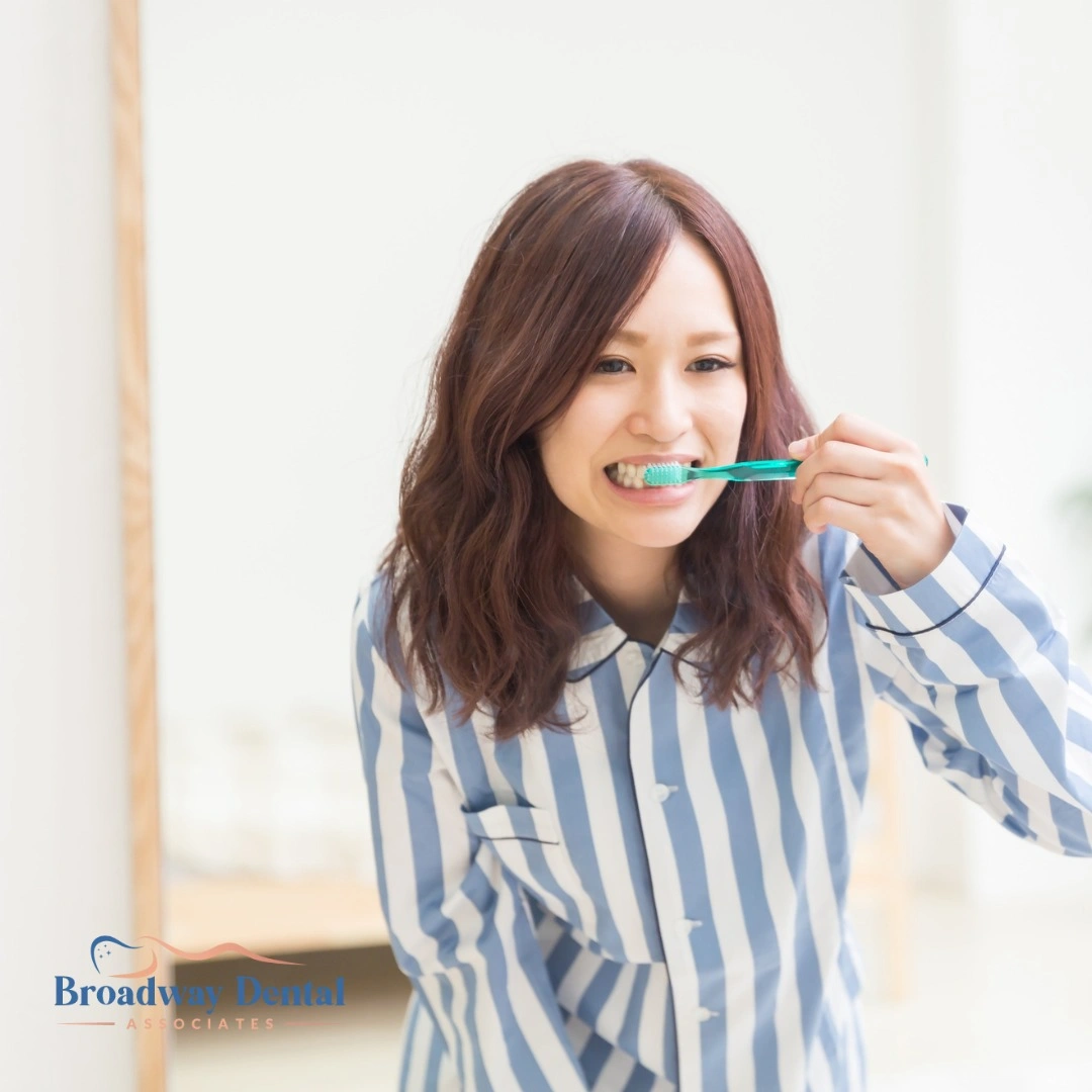 Woman in striped pajamas brushing teeth and Broadway Dental Associates logo in the bottom left of the image.