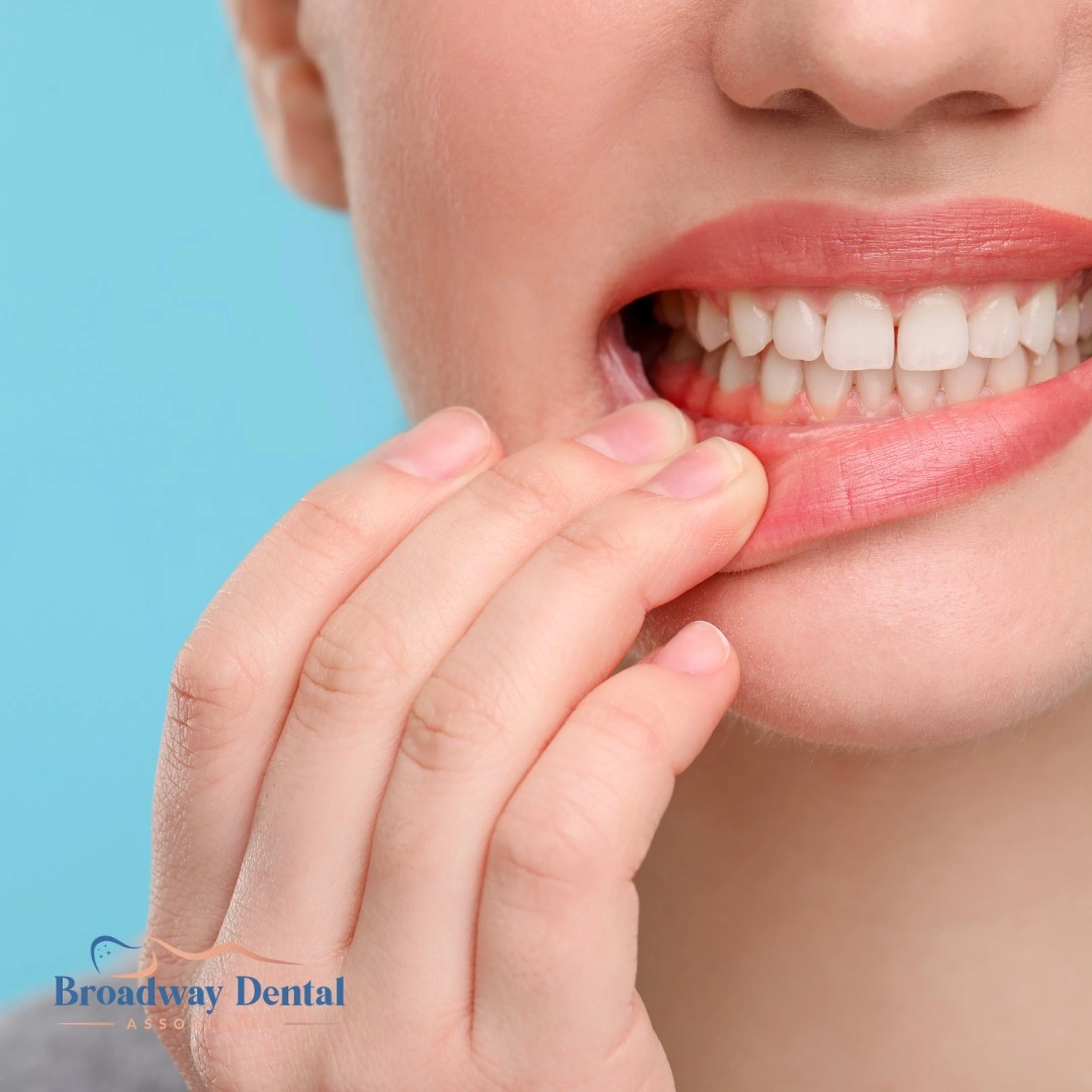 Woman pointing to red gums and Broadway Dental Associates logo in the bottom left of the image
